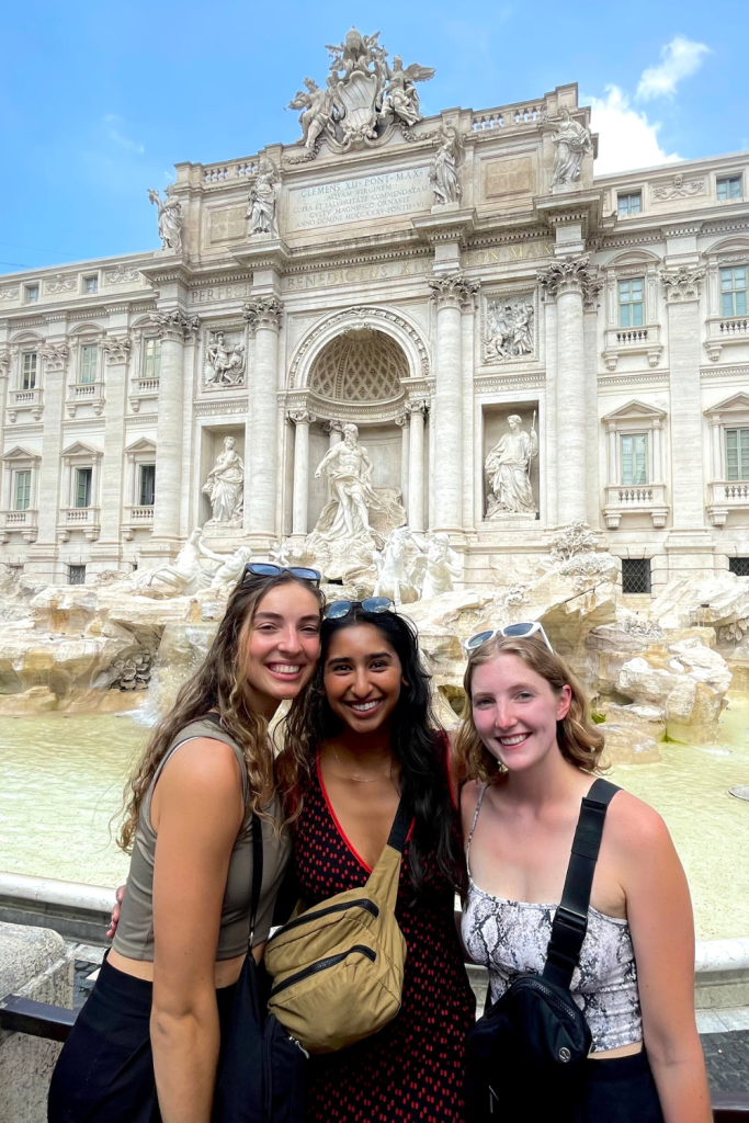 Three best friends enjoying the view of the Trevi Fountain in Rome, Italy on a sunny day while backpacking through Europe after university graduation.
