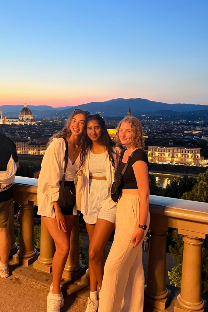Three best friends smiling during a gorgeous pink and yellow sunset at Piazzale Michelangelo in Florence, Italy
