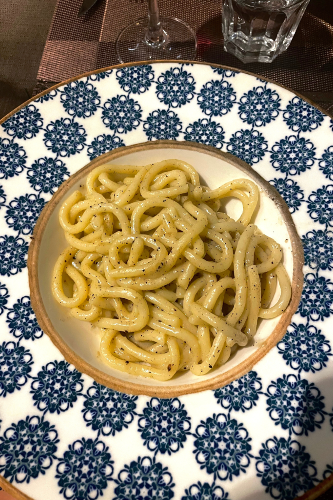 Cacio e pepe made with buccatini noodles, plated in a gorgeous blue and white ceramic bowl, at a restaurant in Florence, Italy