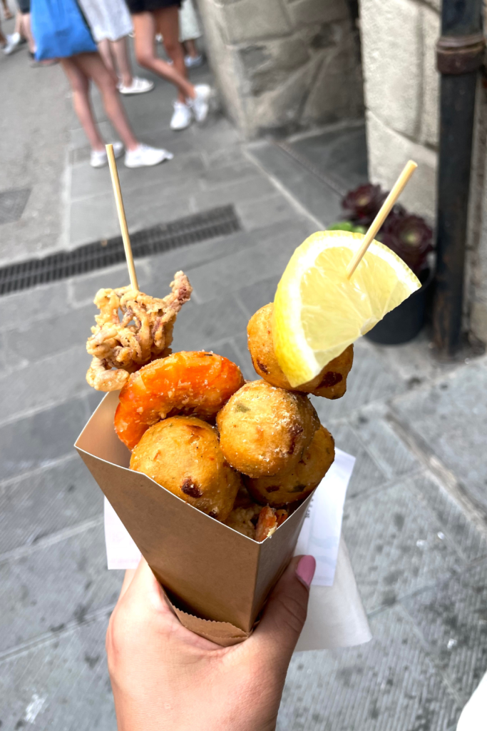 A hand holding a cone filled with fried calamari, shrimp, and crab balls on the streets of Riomaggiore in Cinque Terre, Italy