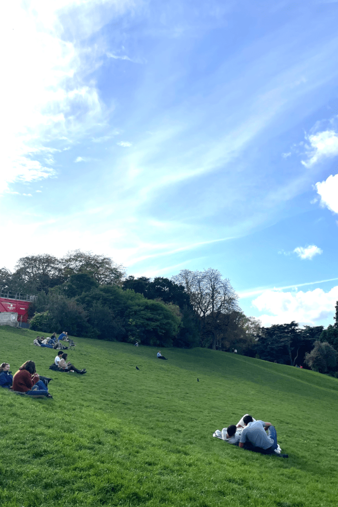 Groups of friends and couples hanging out on a big hill at Parc des Buttes-Chaumont on a sunny fall day in Paris