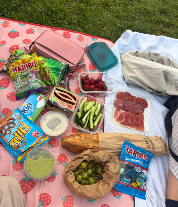 A picnic set up for an out door movie screening at La Villette during the summer in Paris, with a baguette, charcuterie, fruit, veggies, and movie candy.