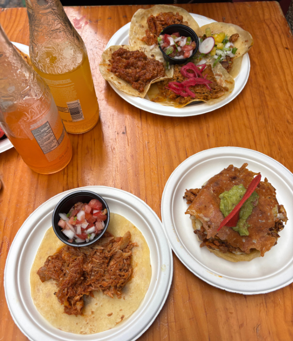 A plate of 4 tacos in the background, and a tinga taco and pastor sopes in the foreground, with two bottles of Jaritos at a delicious Mexican restaurant in Bilbao, Spain