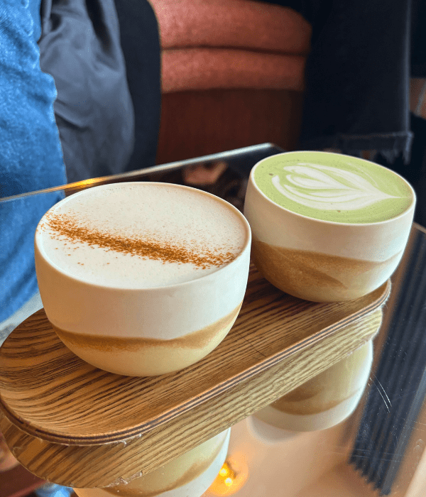 A hot matcha and chai latte served in a smooth, round ceramic mug, plated on a wooden serving board at Noir café in Paris.