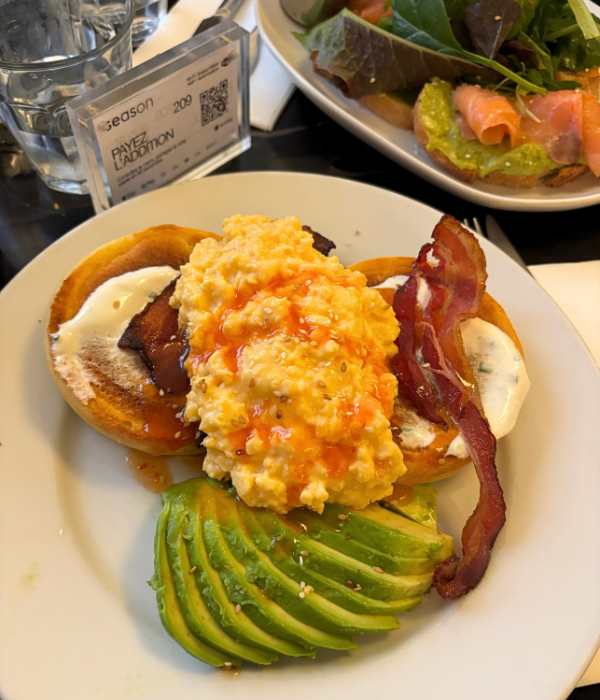 two fluffy pancakes topped with scrambled eggs, avocado and bacon